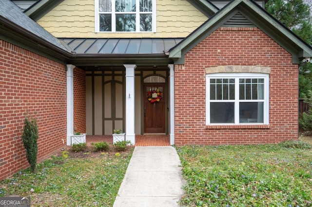 property entrance with a yard, a standing seam roof, brick siding, and metal roof