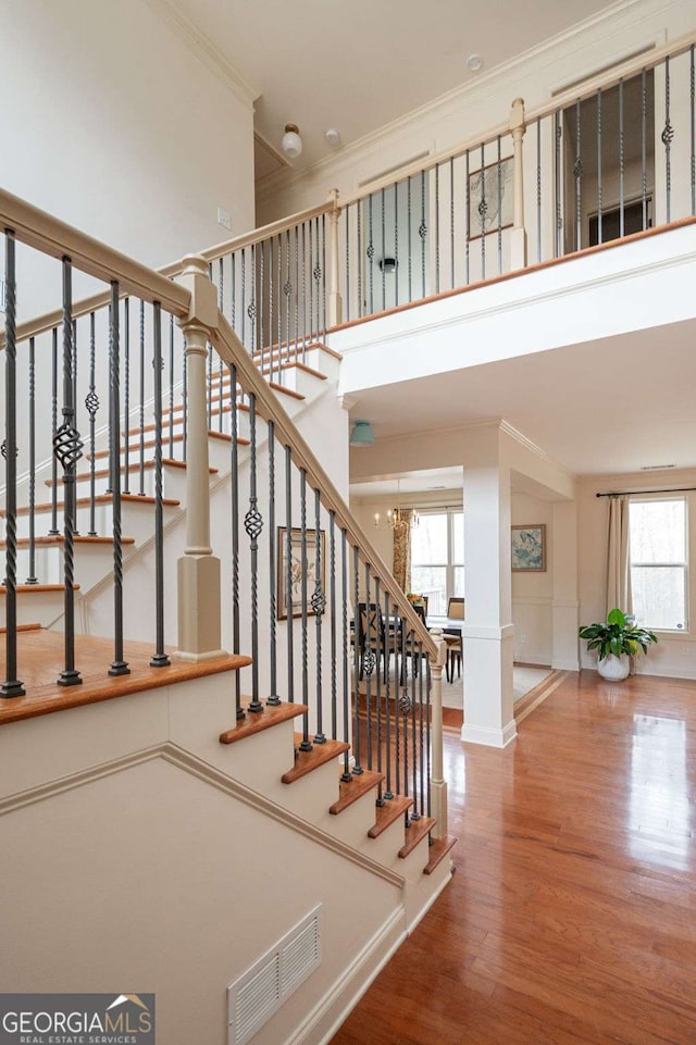 staircase featuring wood finished floors, a towering ceiling, visible vents, ornamental molding, and an inviting chandelier