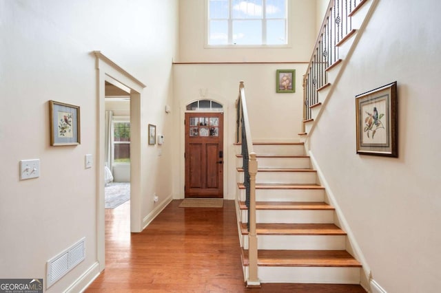 entrance foyer featuring baseboards, visible vents, wood finished floors, stairs, and a high ceiling