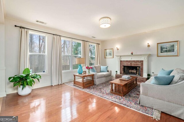 living area with a brick fireplace, baseboards, visible vents, and wood finished floors