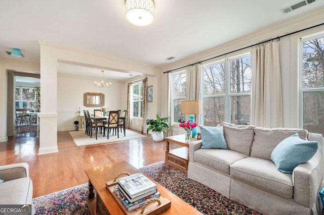 living room with baseboards, visible vents, ornamental molding, wood finished floors, and a notable chandelier