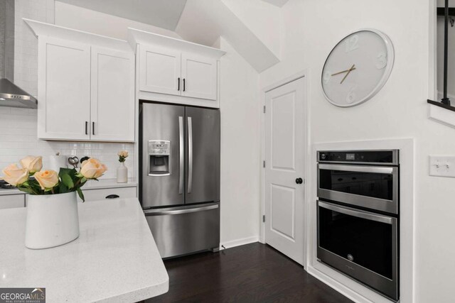 kitchen featuring tasteful backsplash, white cabinets, dark wood finished floors, appliances with stainless steel finishes, and wall chimney range hood