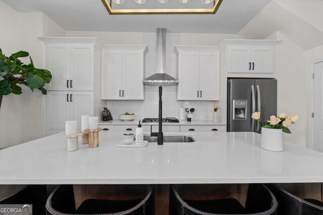 kitchen with a large island, decorative backsplash, white cabinets, wall chimney range hood, and stainless steel fridge with ice dispenser