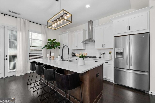 kitchen with a sink, visible vents, wall chimney range hood, stainless steel refrigerator with ice dispenser, and a center island with sink