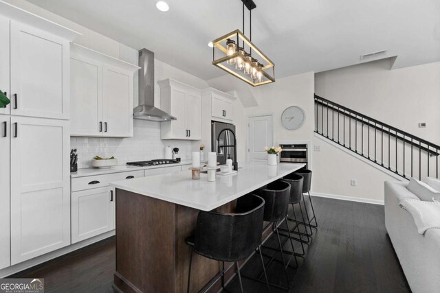 kitchen featuring tasteful backsplash, wall chimney exhaust hood, appliances with stainless steel finishes, light countertops, and white cabinetry