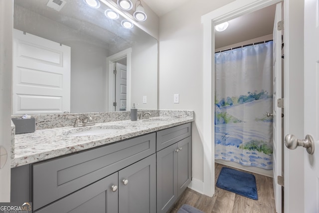 full bath with double vanity, visible vents, a sink, and wood finished floors