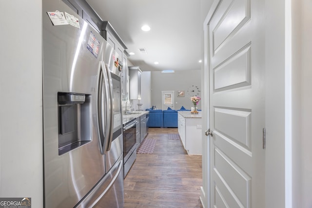 kitchen featuring visible vents, appliances with stainless steel finishes, wood finished floors, light stone countertops, and a sink