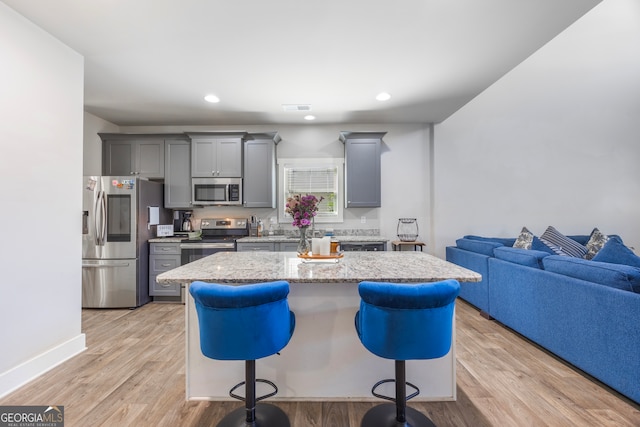 kitchen with appliances with stainless steel finishes, a breakfast bar area, gray cabinets, and visible vents