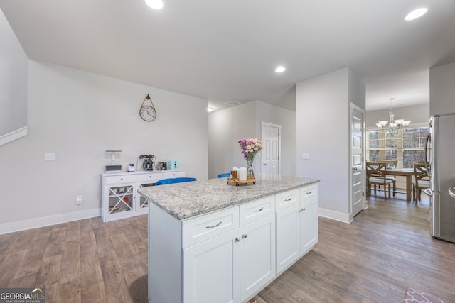 kitchen with white cabinets, baseboards, freestanding refrigerator, a center island, and light wood finished floors