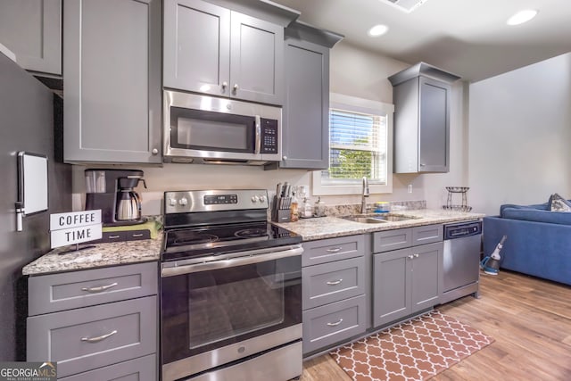 kitchen with light wood-type flooring, gray cabinets, stainless steel appliances, and a sink