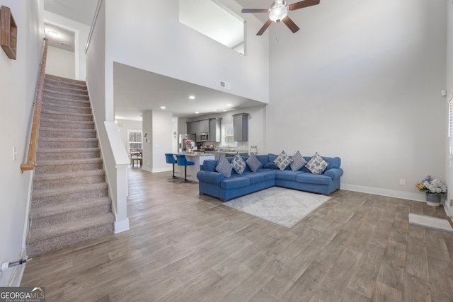 living area featuring visible vents, stairway, light wood-style floors, a ceiling fan, and baseboards