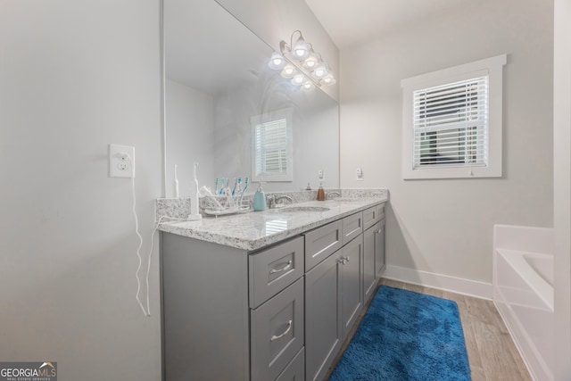 bathroom featuring a tub to relax in, vanity, baseboards, and wood finished floors