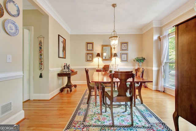 dining room with light wood finished floors, visible vents, and crown molding