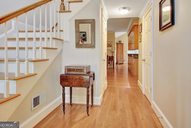 hallway featuring visible vents, baseboards, stairs, ornamental molding, and light wood finished floors