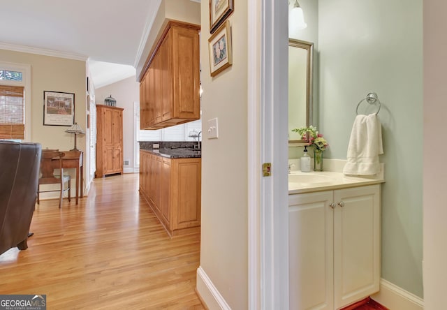 hall featuring baseboards, light wood finished floors, a sink, and crown molding