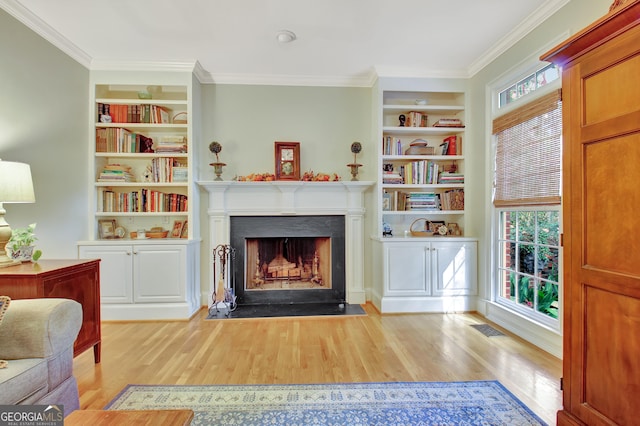 sitting room with a fireplace with flush hearth, built in shelves, ornamental molding, and wood finished floors