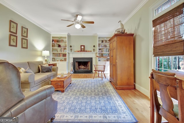 living area with a fireplace, a ceiling fan, baseboards, light wood-style floors, and crown molding