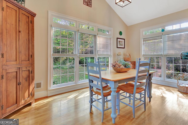 dining area featuring high vaulted ceiling, light wood finished floors, visible vents, and a wealth of natural light