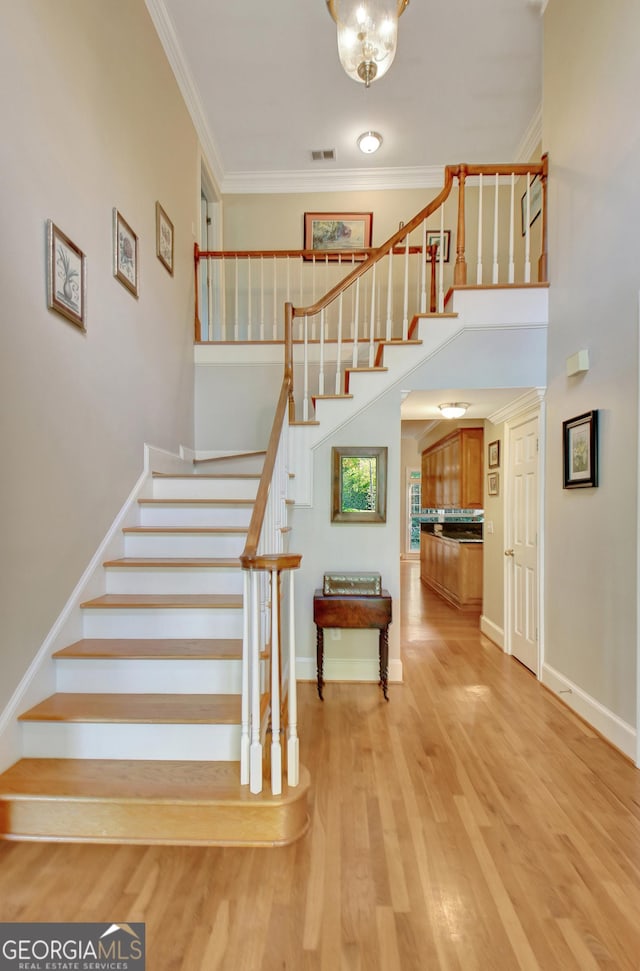 staircase featuring a high ceiling, baseboards, crown molding, and wood finished floors