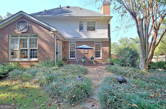 back of house with brick siding, a patio, and a chimney