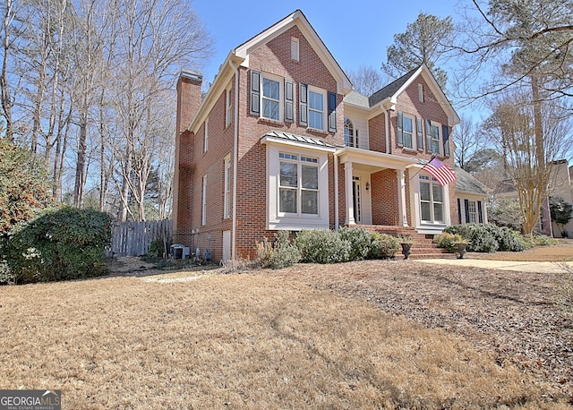 traditional home with central AC, brick siding, a chimney, and fence