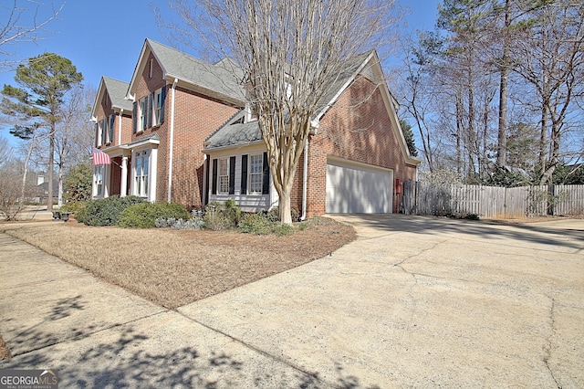 view of side of home featuring a garage, concrete driveway, brick siding, and fence