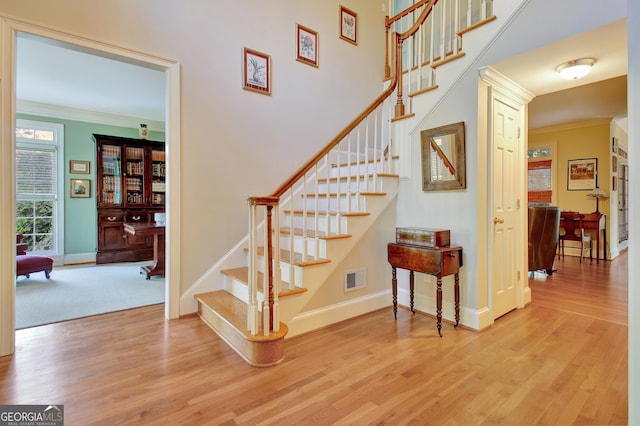 stairway featuring baseboards, wood finished floors, visible vents, and crown molding