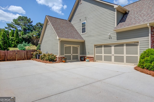 view of side of property with roof with shingles, fence, and an attached garage