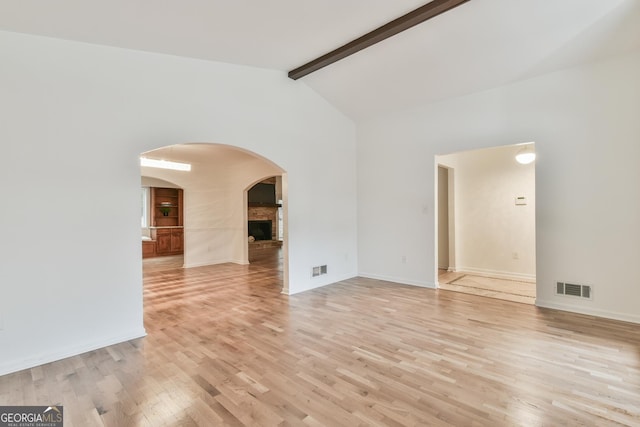 spare room with visible vents, beam ceiling, arched walkways, light wood-style floors, and a brick fireplace