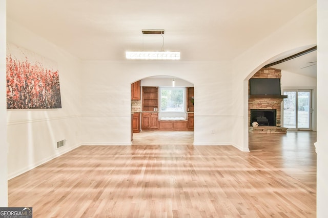 unfurnished dining area featuring plenty of natural light, arched walkways, a stone fireplace, and light wood-style flooring