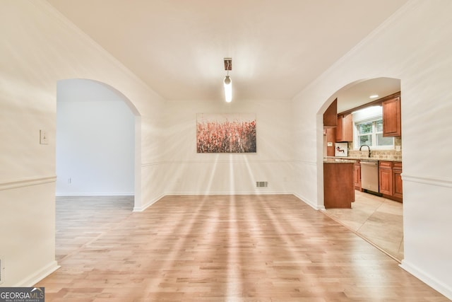 unfurnished dining area with crown molding, baseboards, arched walkways, and light wood-type flooring