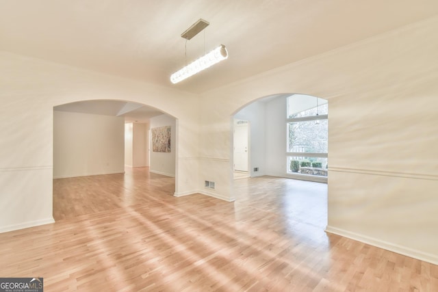 empty room with baseboards, light wood-type flooring, arched walkways, and visible vents