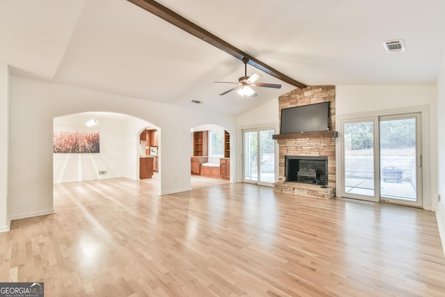 unfurnished living room with visible vents, light wood-style flooring, a ceiling fan, lofted ceiling with beams, and a stone fireplace