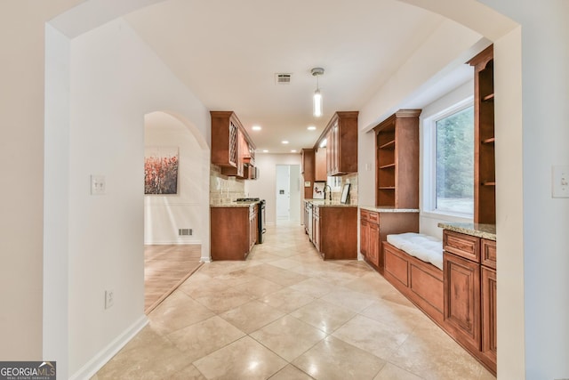 kitchen with stainless steel gas range oven, visible vents, open shelves, arched walkways, and light stone countertops