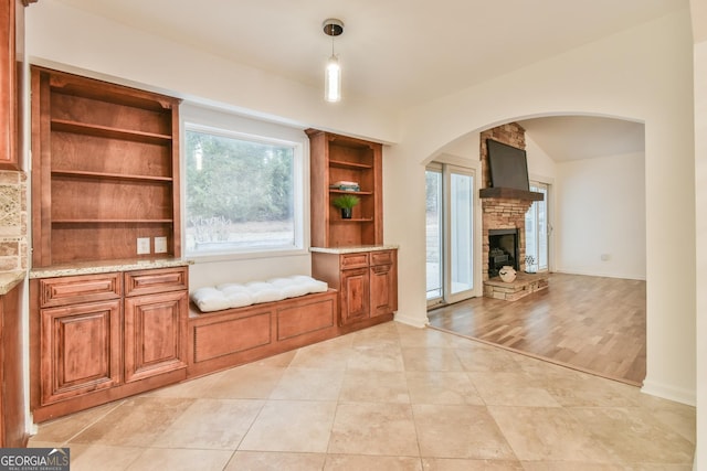 interior space with a stone fireplace, brown cabinets, light stone countertops, and open shelves