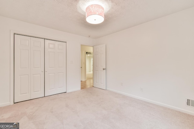 unfurnished bedroom featuring visible vents, baseboards, a closet, a textured ceiling, and carpet flooring