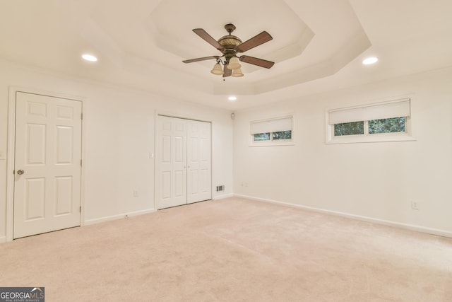 unfurnished bedroom with recessed lighting, a tray ceiling, baseboards, and light colored carpet