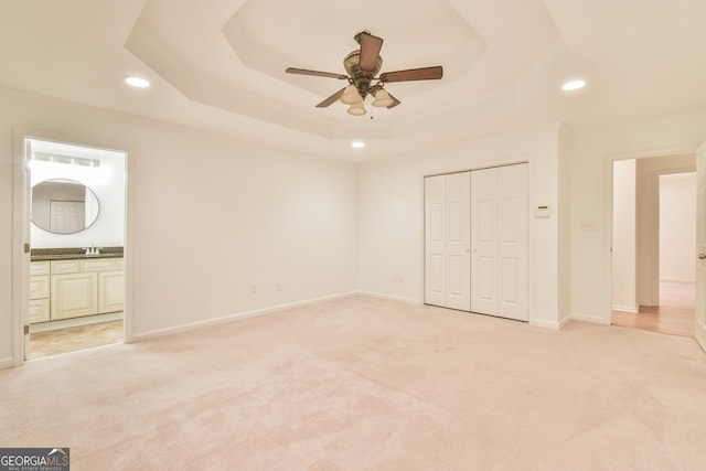 unfurnished bedroom with light carpet, recessed lighting, baseboards, and a tray ceiling