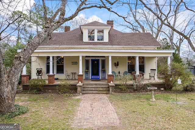 view of front of home with covered porch, a shingled roof, a chimney, and a front lawn