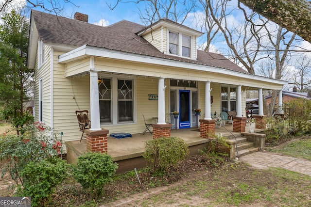 view of front of property featuring a shingled roof, a chimney, and a porch