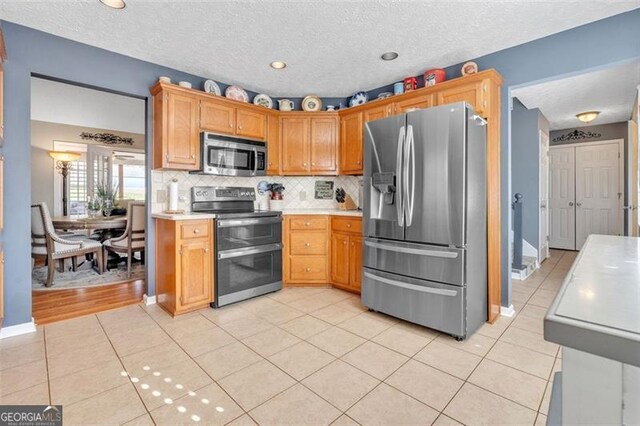 kitchen with light countertops, decorative backsplash, appliances with stainless steel finishes, light tile patterned flooring, and a textured ceiling