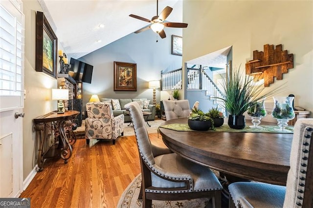 dining area featuring a ceiling fan, wood finished floors, high vaulted ceiling, and stairs