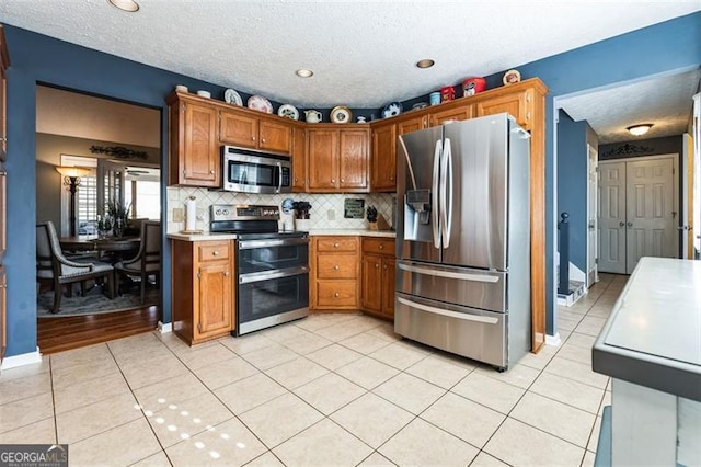 kitchen with light tile patterned flooring, light countertops, appliances with stainless steel finishes, backsplash, and brown cabinetry