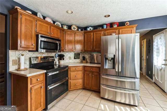 kitchen featuring stainless steel appliances, light countertops, decorative backsplash, brown cabinetry, and light tile patterned flooring