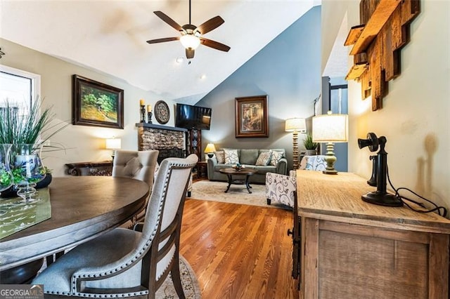 dining area featuring lofted ceiling, ceiling fan, a stone fireplace, and wood finished floors