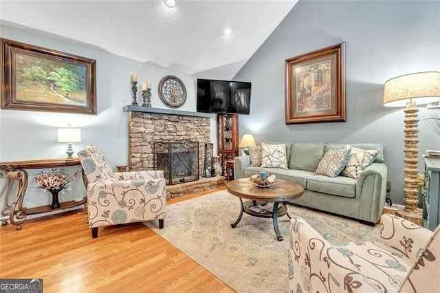 living area featuring lofted ceiling, a stone fireplace, recessed lighting, and wood finished floors