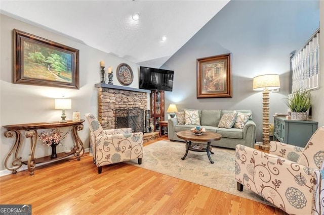 living room featuring lofted ceiling, a stone fireplace, baseboards, and wood finished floors