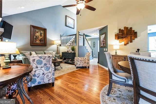 living room with stairway, a ceiling fan, high vaulted ceiling, light wood-type flooring, and baseboards