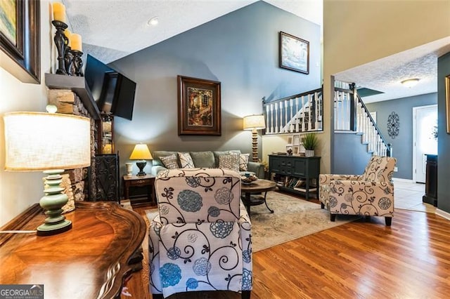 living area featuring high vaulted ceiling, a textured ceiling, stairway, and wood finished floors