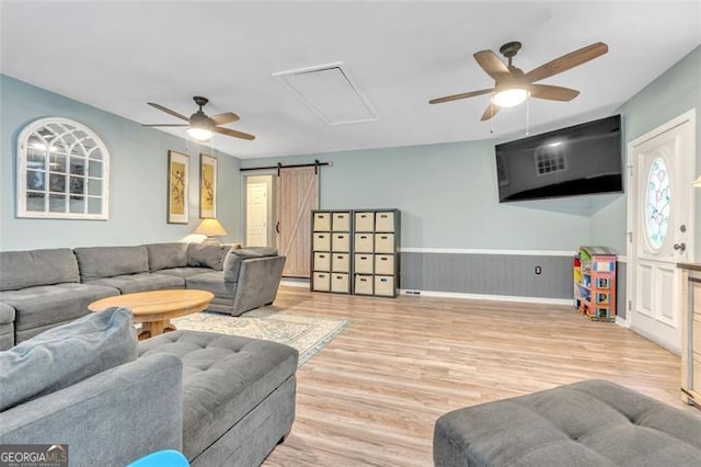 living room featuring a wainscoted wall, a barn door, ceiling fan, and wood finished floors